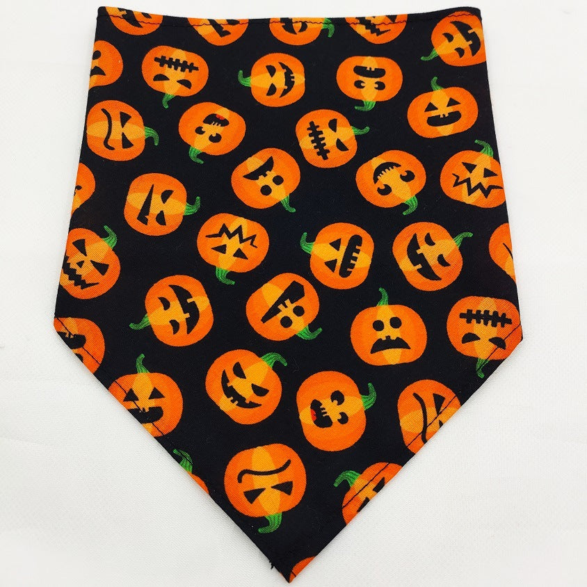 Black fabric Pet Tie-Dye Triangle Bandana Scarf for Dogs & Cats featuring an all-over pattern of various orange jack-o'-lantern faces with green stems.