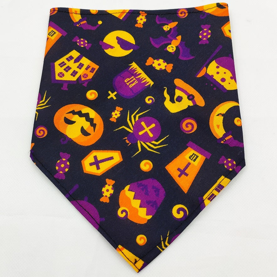 Pet Tie-Dye Triangle Bandana Scarf for Dogs & Cats with a Halloween-themed pattern featuring pumpkins, spiders, haunted houses, and candy in bright orange, purple, and yellow colors.